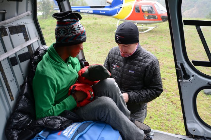 A mountain rescue medic attends to a rescued climber in a helicopter on the ground.