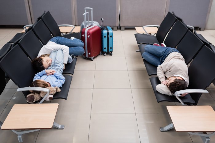 A family sleeps on chairs in an airport terminal.