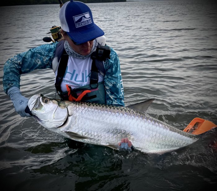 A fishing woman standing in the water holds a large silver fish she caught.