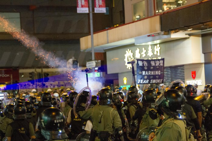 A large unit of law enforcement personnel shoot tear gas into a protesting crowd in an Asian city.