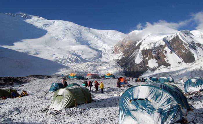 Un grupo de personas en torno a un campamento base a gran altitud bajo un pico nevado.  