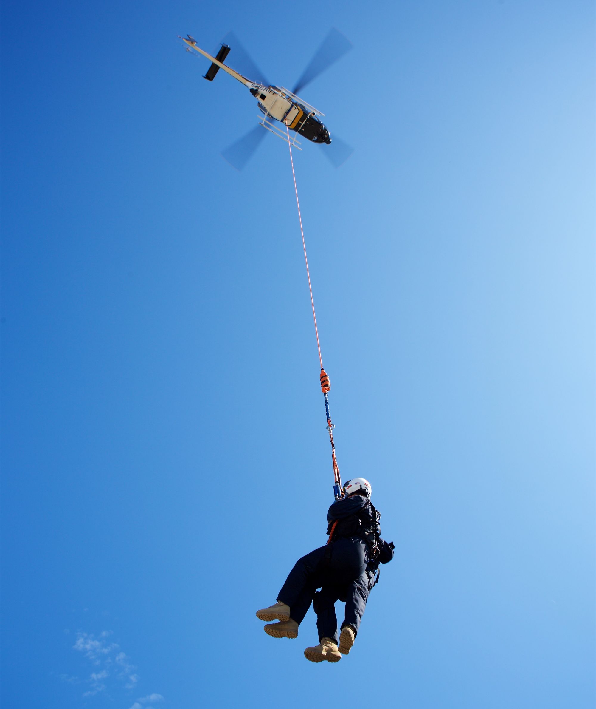 Un piloto de evacuación médica eleva a un herido a través de una larga cuerda por debajo de un helicóptero en vuelo estacionario.