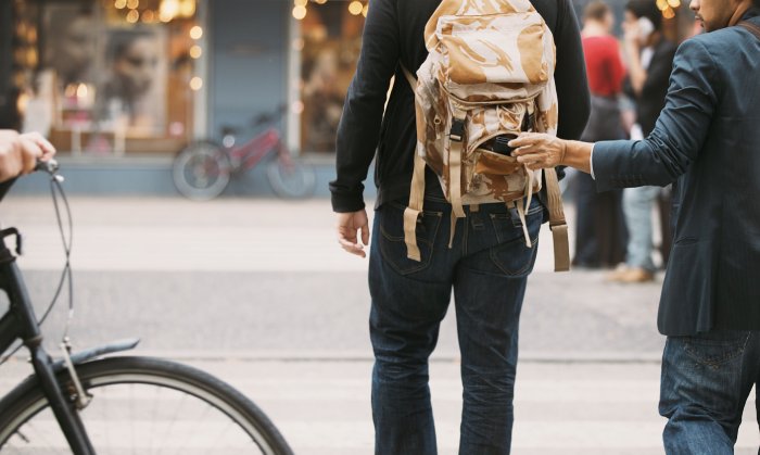 A man steals a wallet from the open backpack worn by another man.