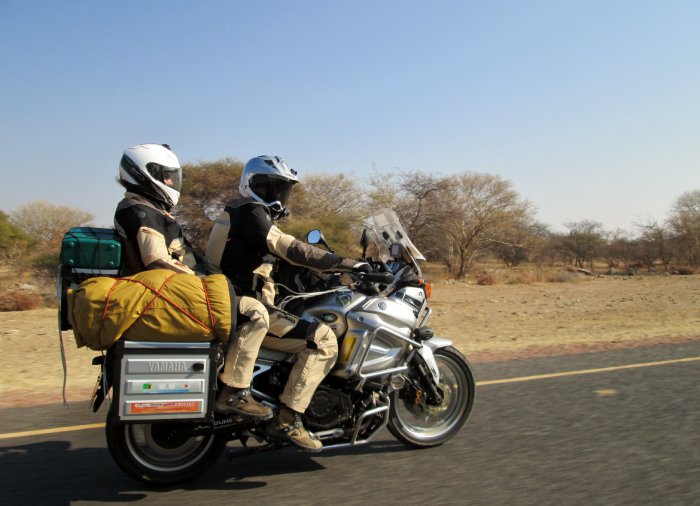 Two people ride on a motorcycle in the Namibian desert.