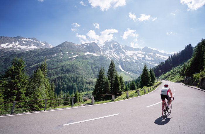 A road cyclists rides along a winding Alpine road in Italy on a sunny day.