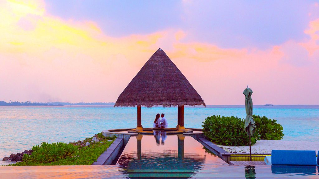 Honeymoon couple under a tiki hut on a private beach with an infinity pool
