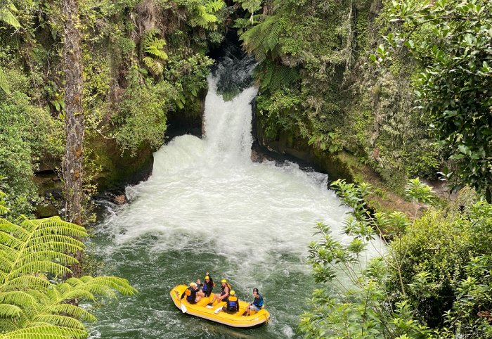 A waterfall empties into a river where a whitewater raft with people on board look on.