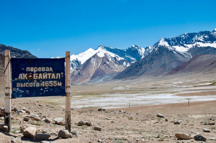 Una señal de tráfico, una pradera y montañas nevadas bajo un cielo azul.