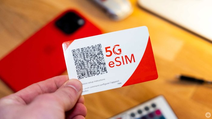 A hand holds a red and white eSIM card above a table with a red smartphone on it.