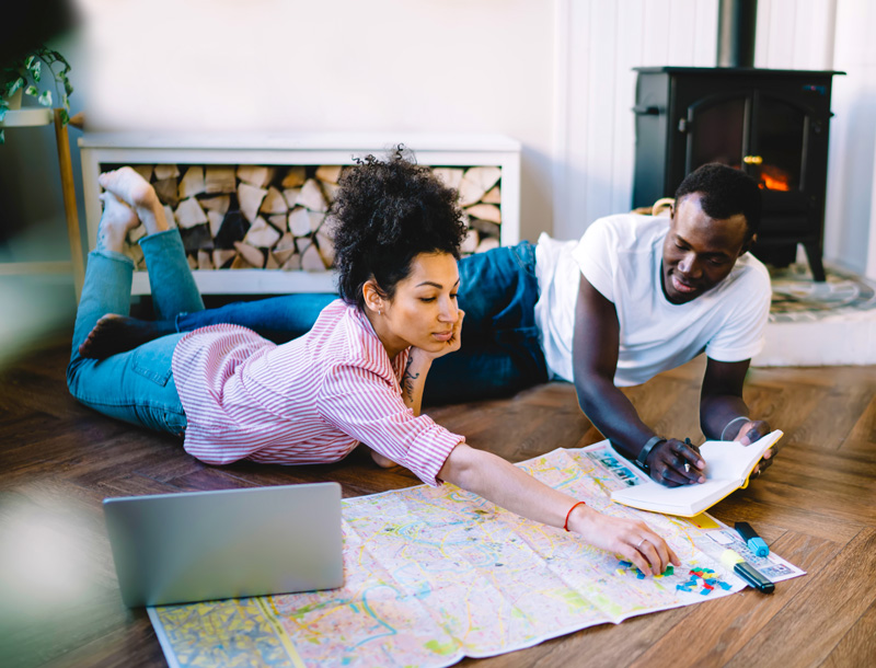 couple laying on the floor with a map and laptop planning vacation together