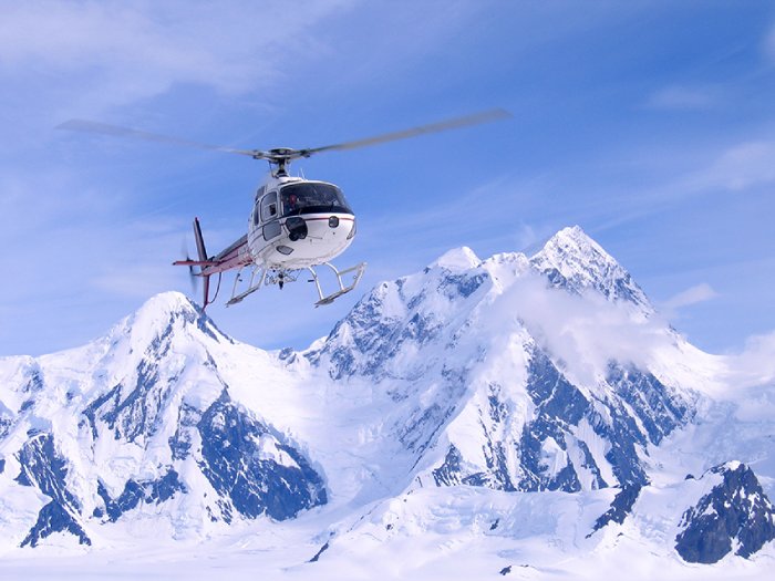 A helicopter approaches a landing in high, snowy mountains.