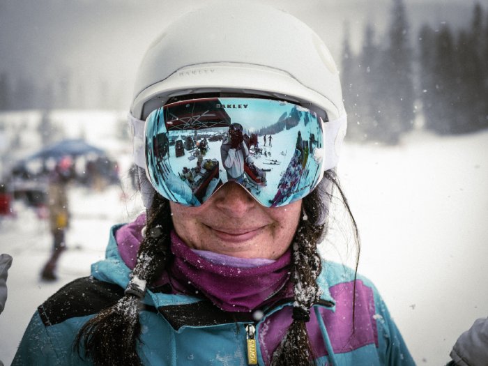 A female snowboarder wearing white helmet, mirror goggles, and blue and purple outfit.