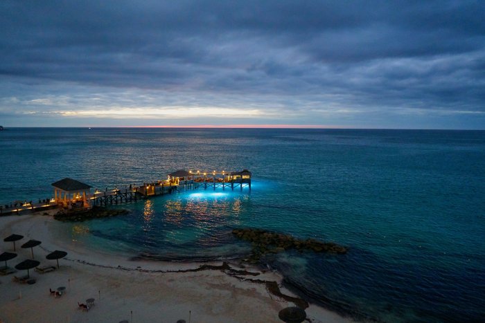A pier lit up above light blue water at dusk in the Bahamas.