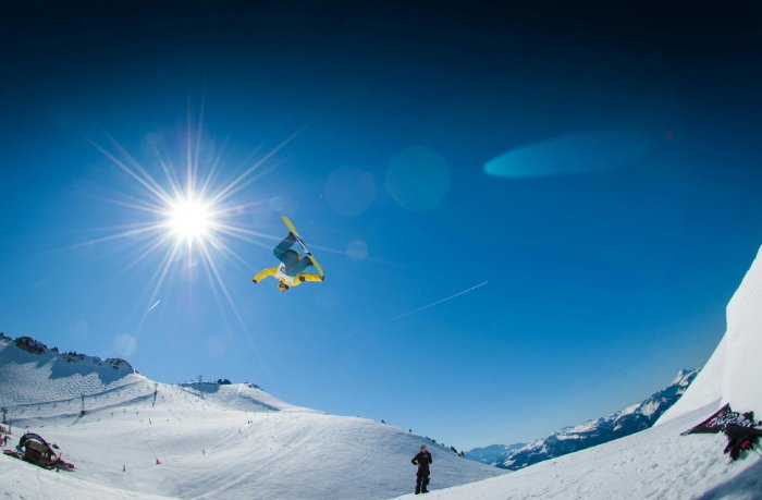 A snowboarder performs a trick under a bright sun.