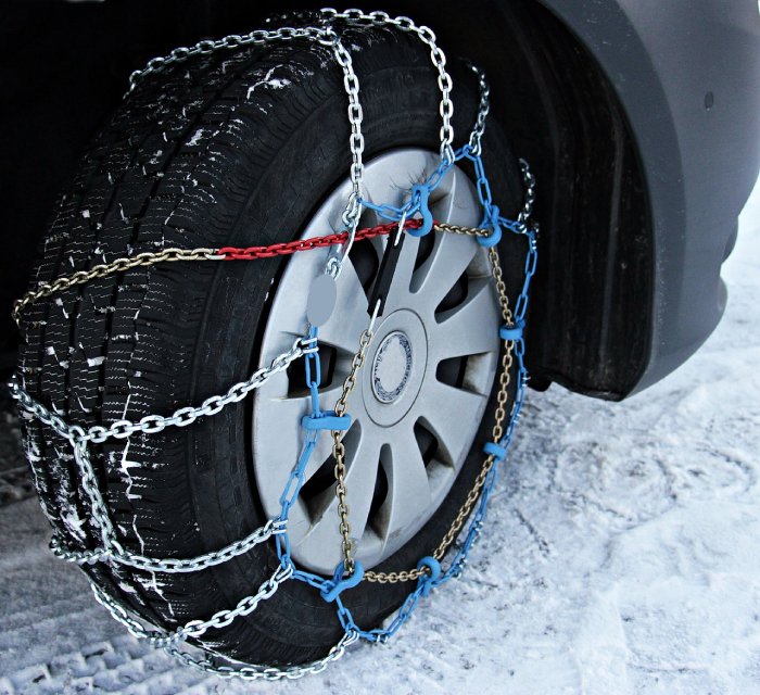 A close-up of a car's snow tire with chains on it.