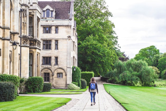 A young woman student walks along a college campus green.