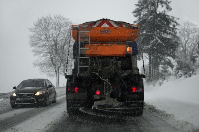 A large snow plow truck spreads salt on a snowy road.